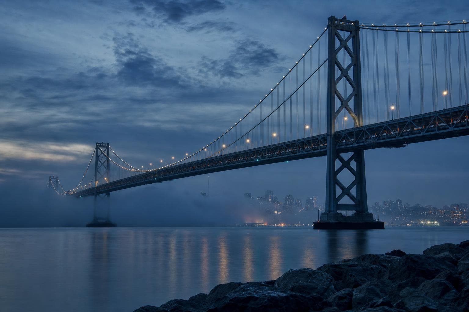 A steel suspension bridge crossing still water at dusk